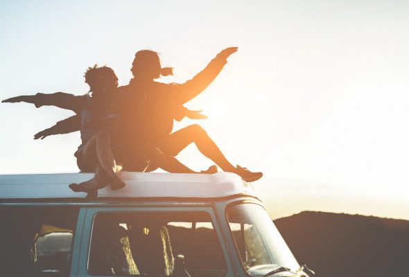 Happy couple silhouette sitting on top of minivan at sunset - Young people having fun on summer vacation traveling around the world - Travel, love, van lifestyle, concept - Focus on bodies